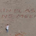 Steine sind auf dem Sand zu einem Schriftzug zusammengelegt: "Kein Plastik ins Meer"